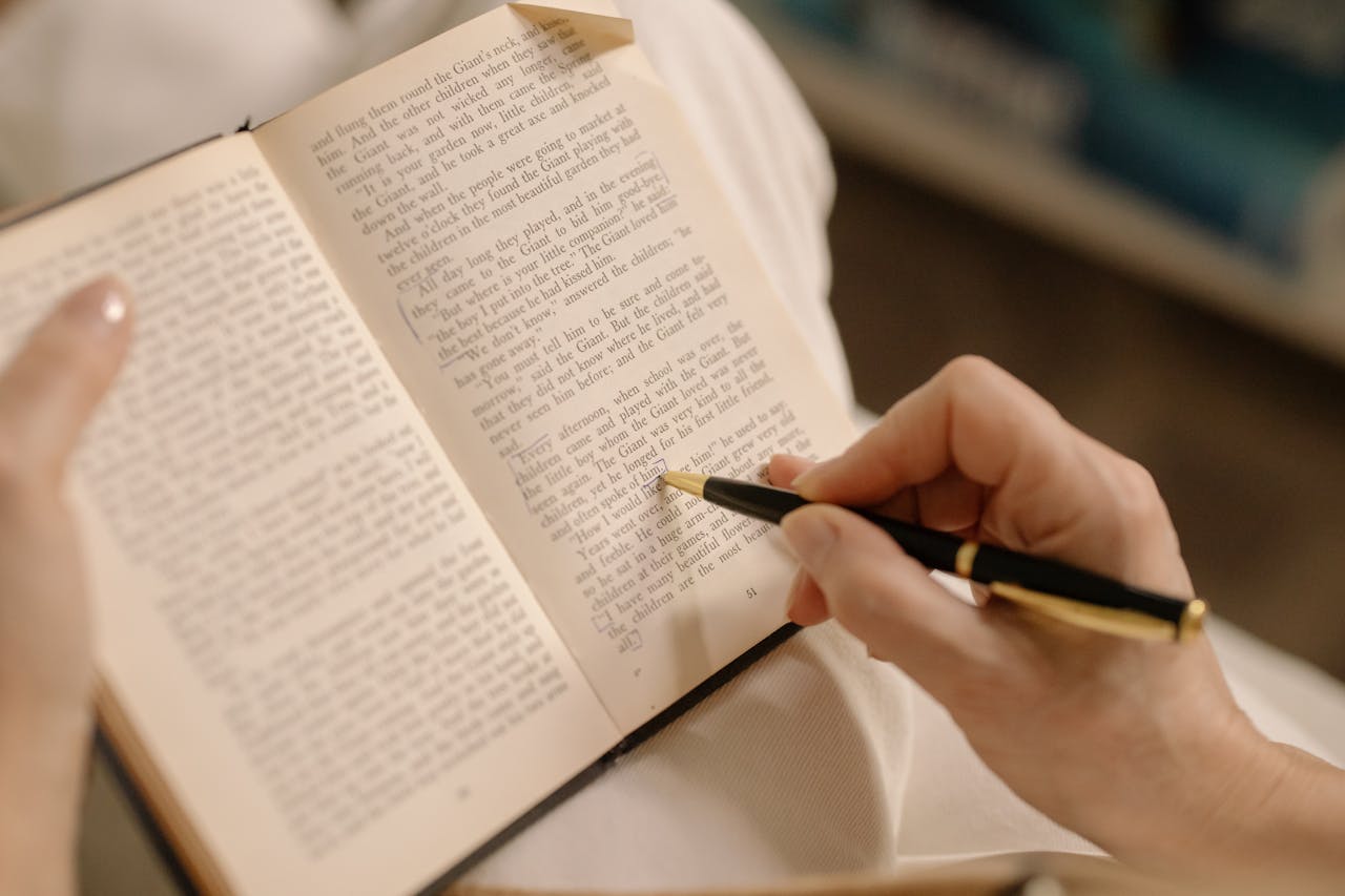 Hands holding a pen and annotating a book page, perfect for study or education themes.
